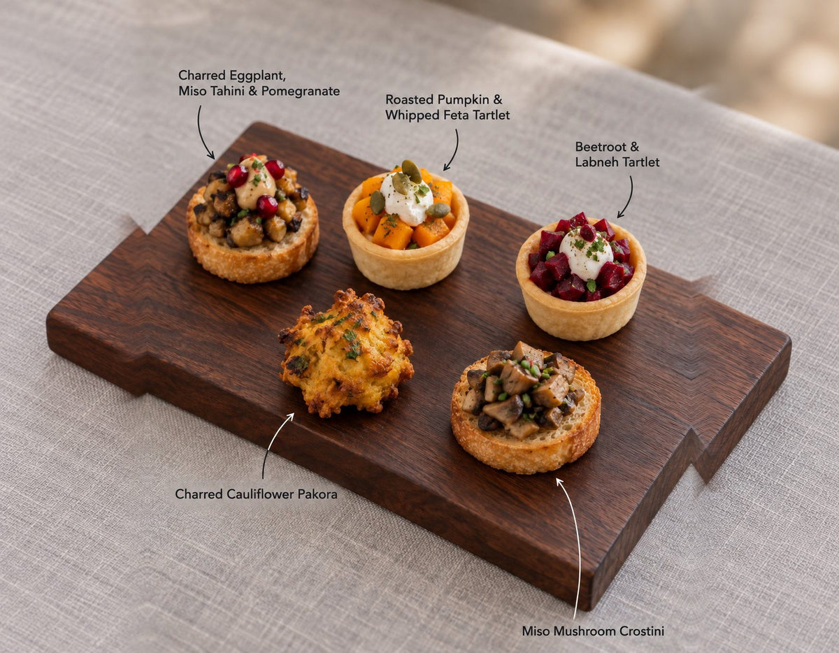 The Garden canapes on a wooden board, labelled Charred Eggplant, Miso Tahini & Pomegranate and 4 more. Cuseho canape catering, Singapore