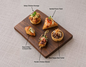 The Singapore Table canapes on a wooden board, labelled Satay Chicken Karaage and 4 more. Cuseho canape catering, Singapore